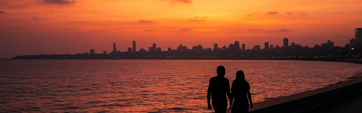 Two distant silhouettes walk beside the Arabian Sea at sunset with Mumbai's skyline beyond.